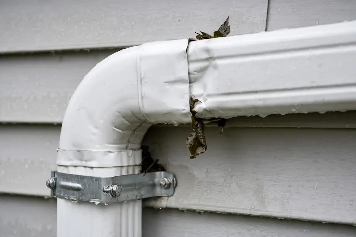 Close-up of a white aluminum downspout elbow joint secured by a bracket on siding