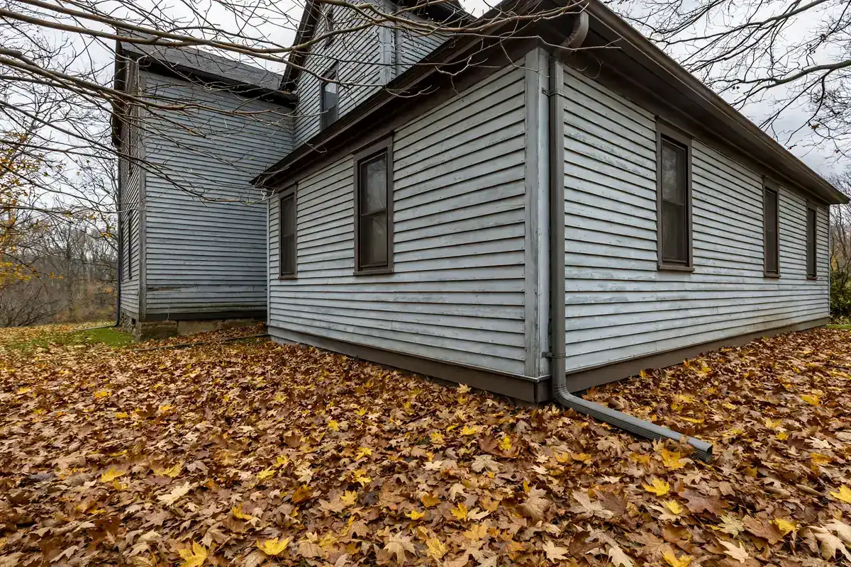 A house corner in autumn with a downspout and extension over a leaf-covered lawn