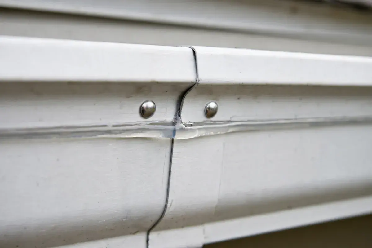 A freshly sealed seam with new rivets on a white aluminum gutter run